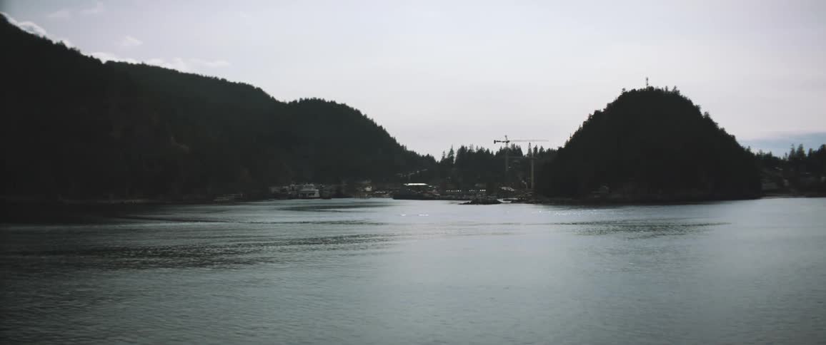 A lake next to cliffs with trees with the sky and clouds in the background