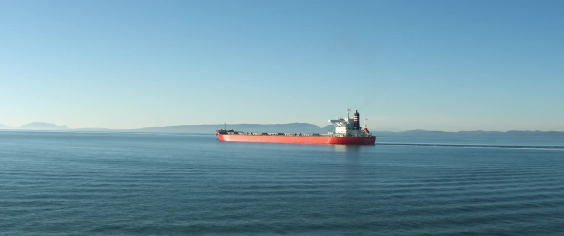 Cargo ship travels in the ocean under a blue sky