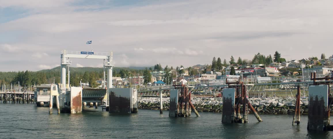 Rail sits over water near marina with town and hills in background under a cloudy sky
