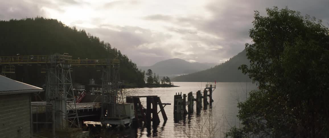 A dock on a lake with trees and mountains the sky and clouds in the background