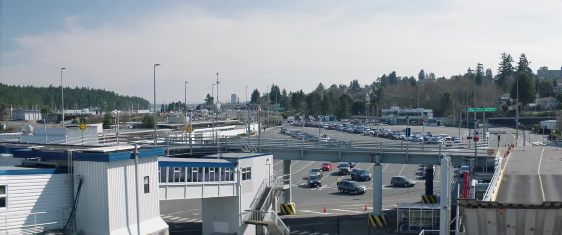 A person in a yellow jacket directs traffic to lead dozens of vehicles out of the parking lot of a business