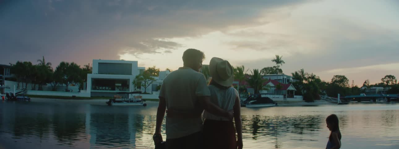 The backside of a man and woman holding each other kissing next to their daughters in front of water