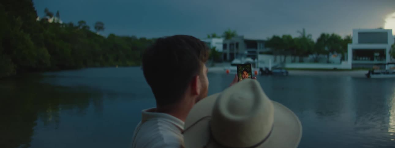 A man holds up his smartphone during a video call with his partner along a lake