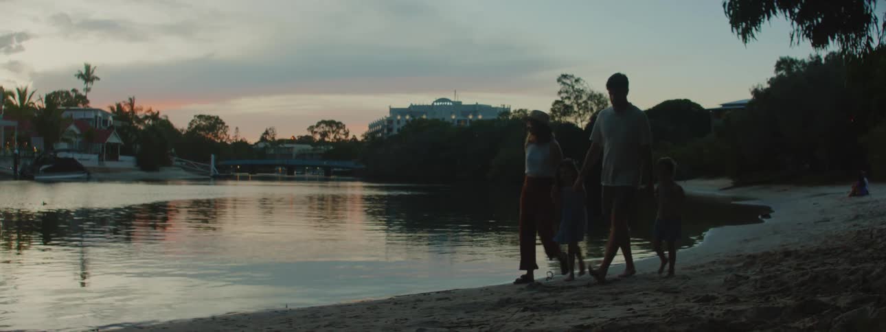A mother father and two daughters holding hands walking on sand next to the shoreline