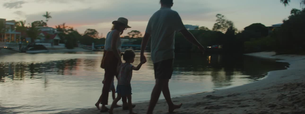 Father mother and daughters holding hands walk along the beach at dusk