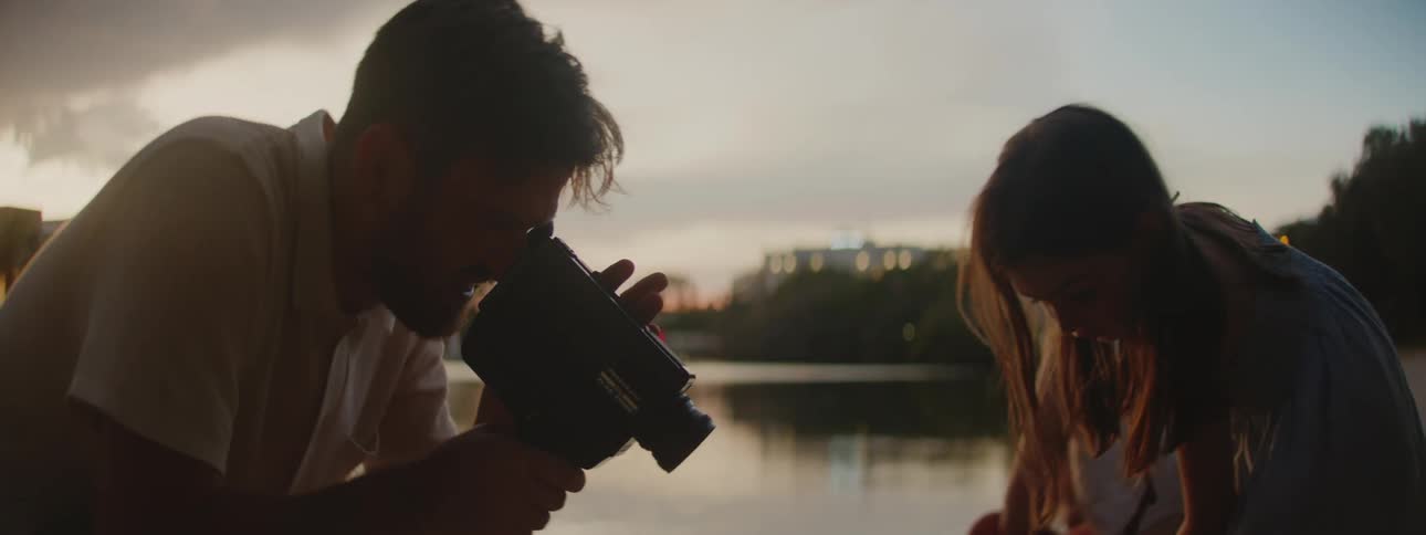 A man records his daughter while she draws in the sand