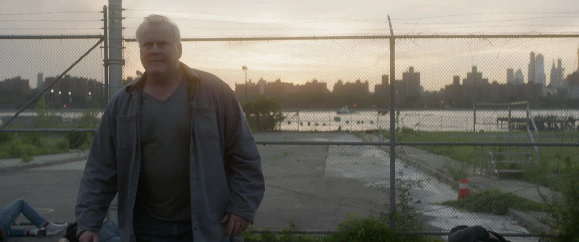 Older man walking away from a fence that has a river and city behind it