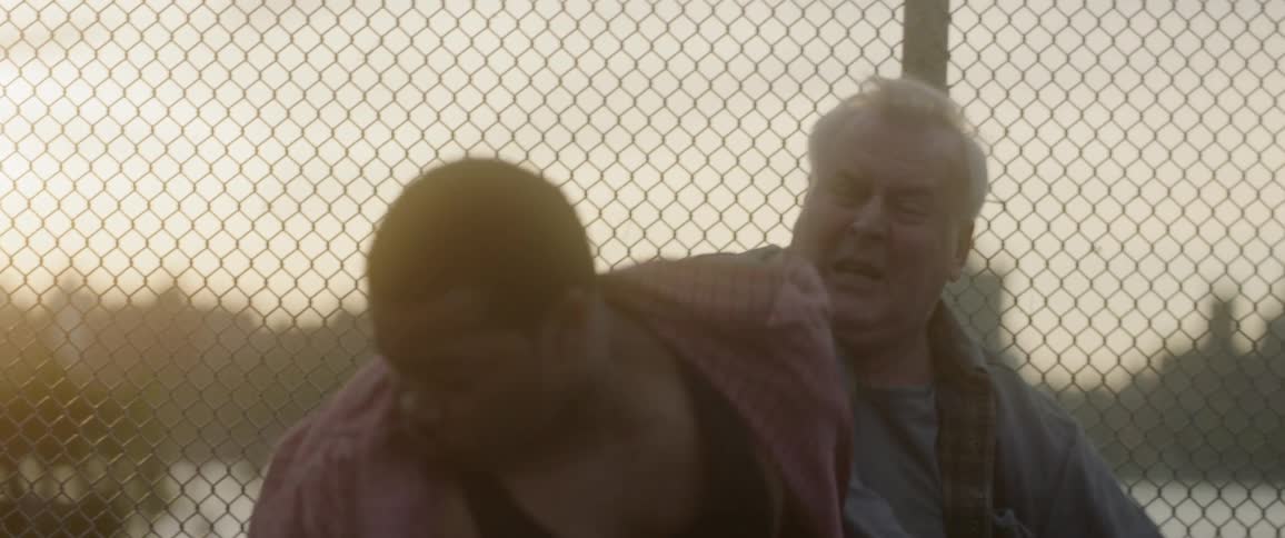 White man hits black man in front of wire fence at sunset