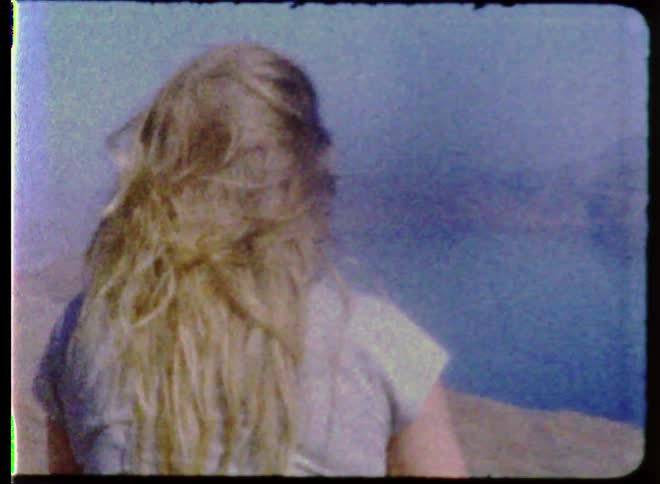 Woman touches hair and looks at a lake