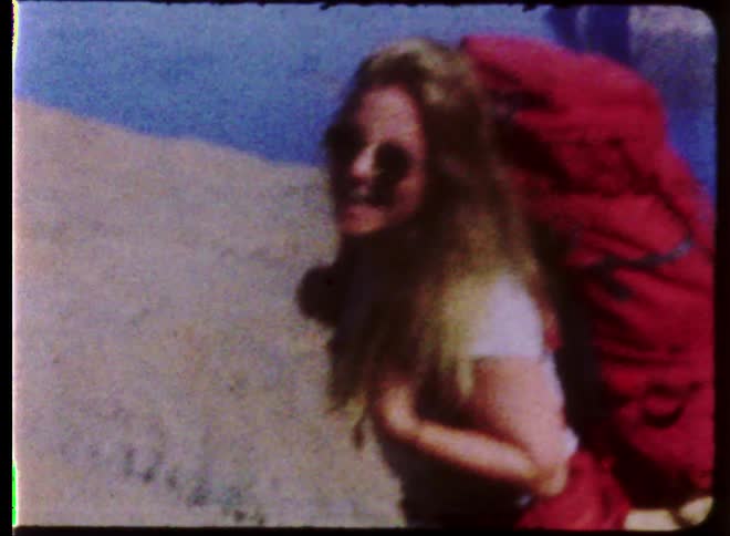 A vintage film of a woman with a red hiking backpack