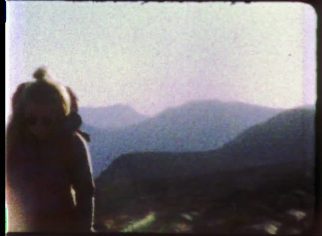 A vintage video of a woman walking up a hill with a backpack on