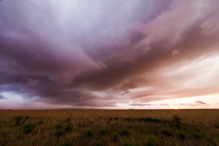 Purple colored clouds move in the sky above an empty field at sunset