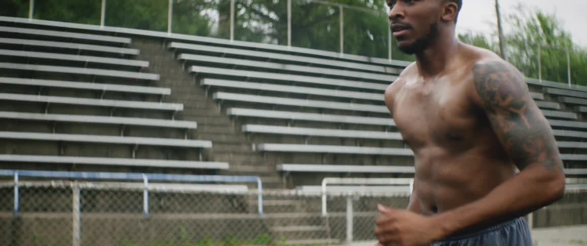 A shirtless man runs on an athletics track during the day