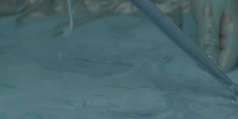 A pair of hands is reaching into a vat of blue liquid and pulling out a drumstick