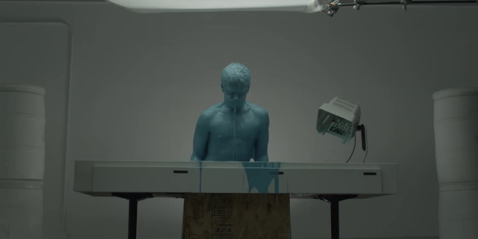 A paint covered man rises from a table