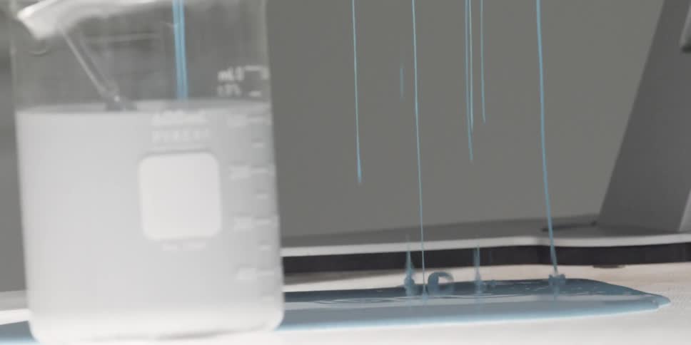 A beaker filled with white liquid and blue liquid dripping behind it