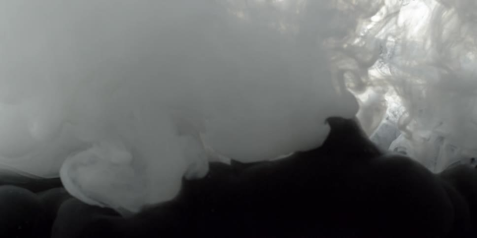 A white liquid billows and spreads in a container