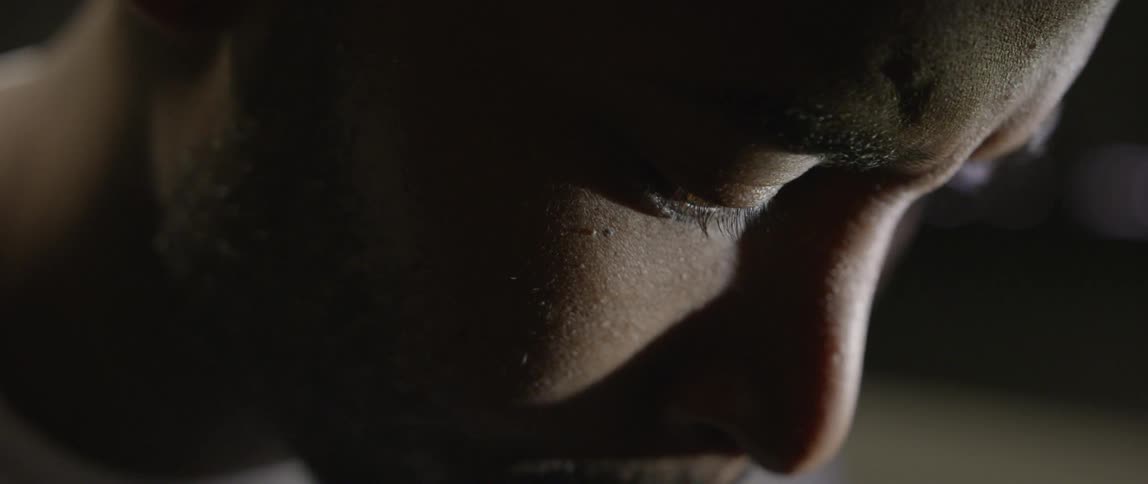 Light passes over the face of a man whose head is bowed
