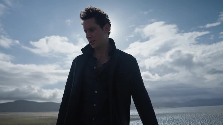 Man wipes his face and looks upset while looking around plain a distance from mountain on sunny day