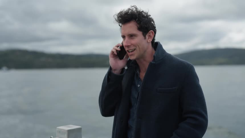 Man stands in back of boat moving away from coast and makes a phone call