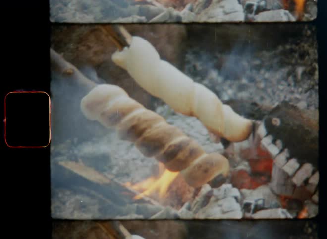 Food on sticks roasts over campfire flames