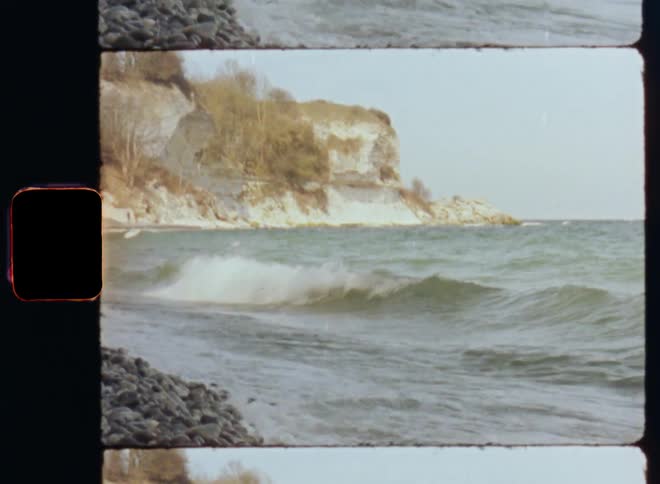 Waves crash onto rock covered shore near white seaside cliff