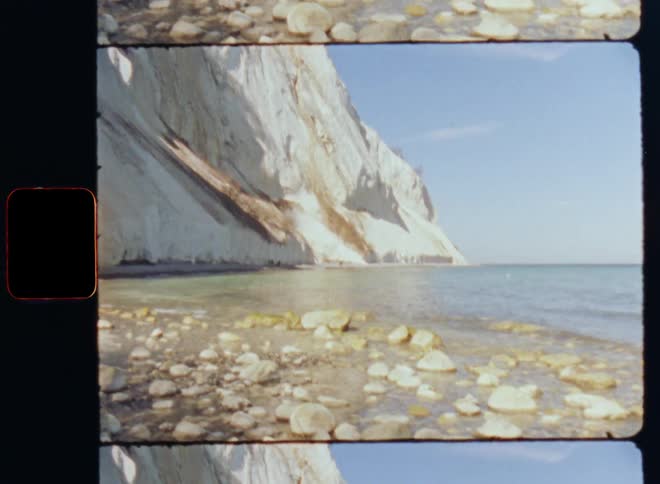 Waves roll onto rock strewn shore a short distance from white seaside cliff