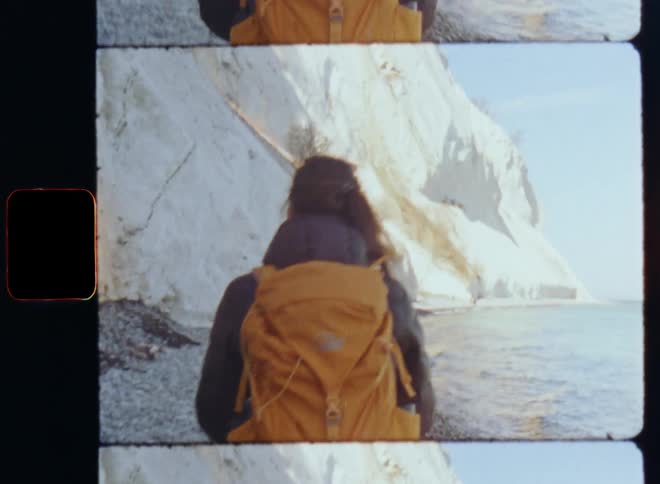 Woman hikes along rocky shore near white cliff