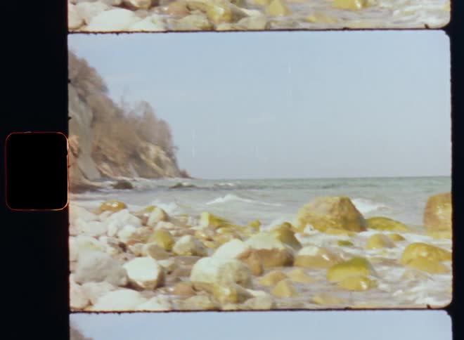 Old footage of sea waves washing up against a rocky coastal shore
