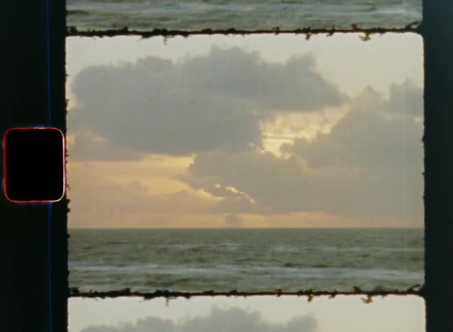 Vintage 8mm fast motion time lapse of the setting sun that shines through clouds over ocean turning horizon red as the water moves and the last daylight disappears