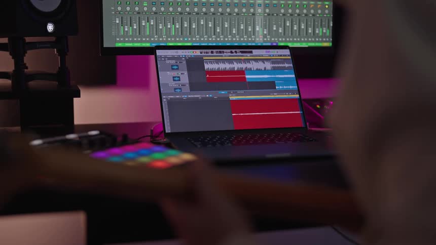 Musician plays string instrument near computers displaying audio information