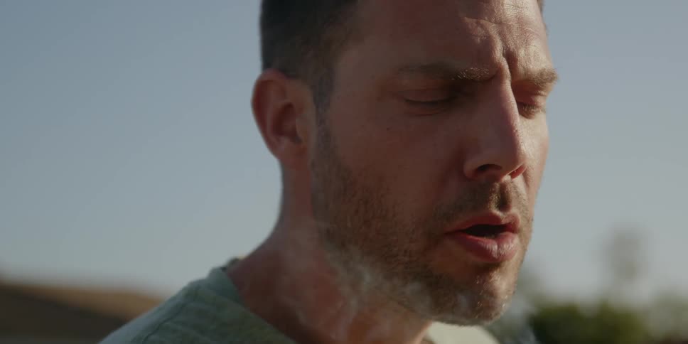 Man stands outdoors under a blue sky smoking
