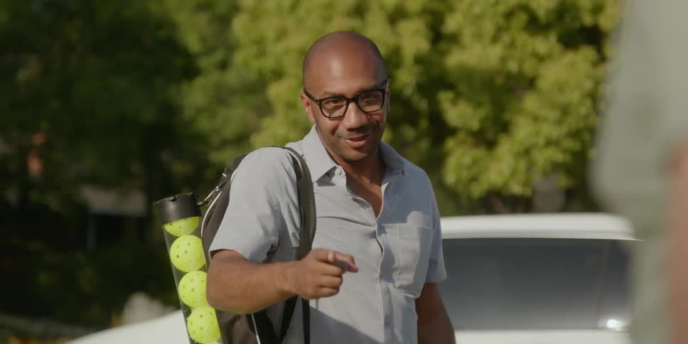 A man carrying a bag of whiffle balls talks to someone holding a cigarette before walking away
