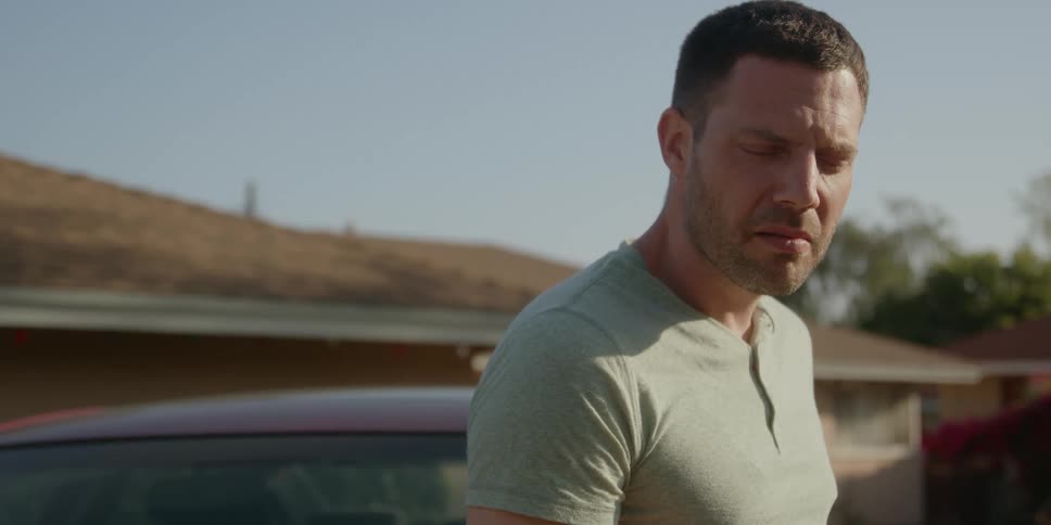 Introspective man standing next to a car in front of a house smoking a cigarette at daytime