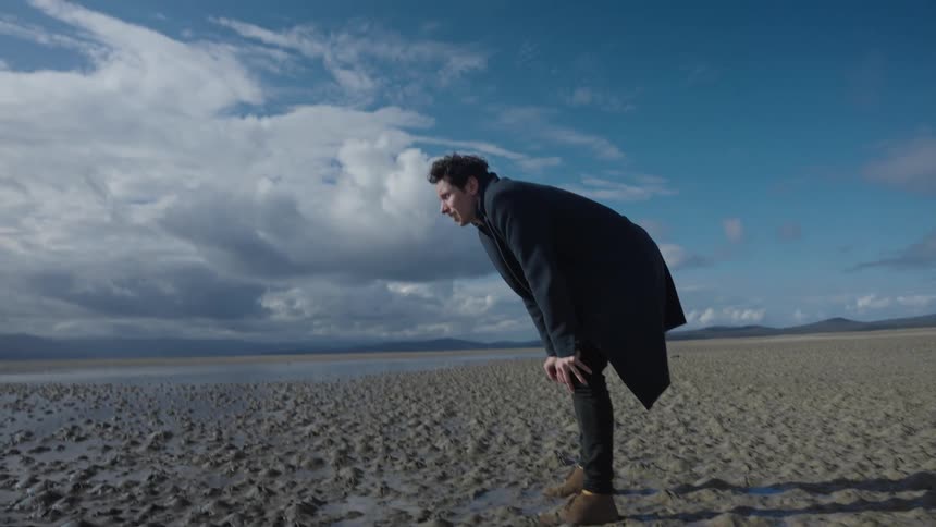 A man walking on a beach bends down and breathes deeply