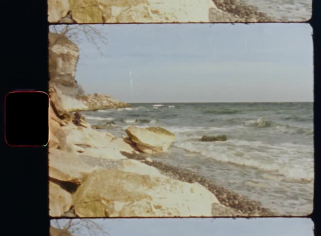 Old footage of gentle waves lapping on a rocky shoreline