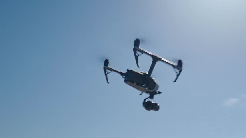 Drone with camera flies over wet sand toward walking man with mountains on the horizon