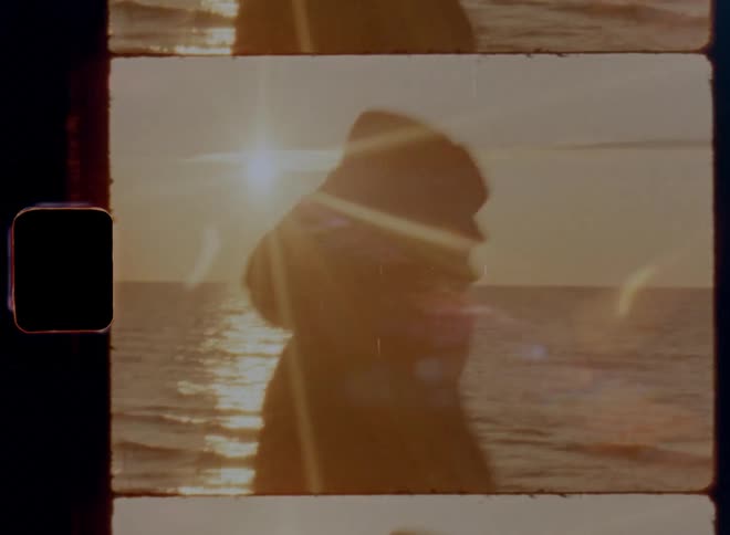 A woman with woollen hat and thick jacket is walking or strolling by the water or ocean in the early morning hours during sunrise or late in the evening at sunset