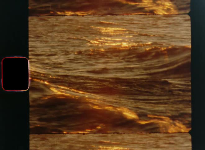 Waves are rolling in or washing up the shoreline or gravel beach as the golden sun is setting at the horizon shining brightly into the vintage camera causing lens flare and the sunshine reflects on the surface of the water