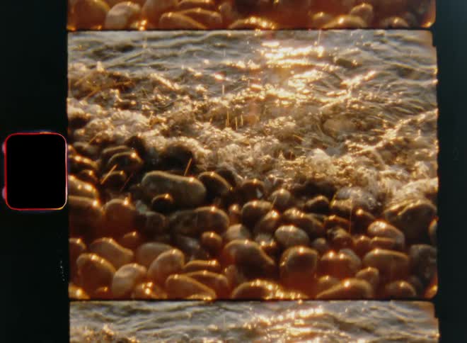 Several rocks are shown with tiny ocean waves washing over them as the moving water splashes while reflecting the bright sunlight of the warm and golden shining sun
