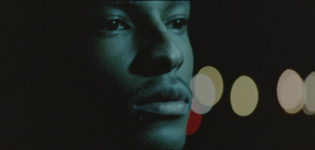 A man standing in front of bright lights at night lifts his head up