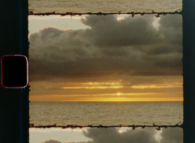 Super 8 mm timelapse or fast motion of the setting sun with clouds moving during a stunning sunset over the ocean or sea by the beach as the shining sun goes down at the horizon