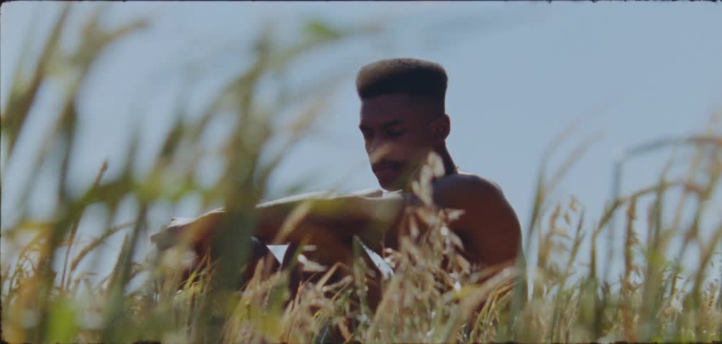 Shirtless black man sitting on a grass field on a sunny day