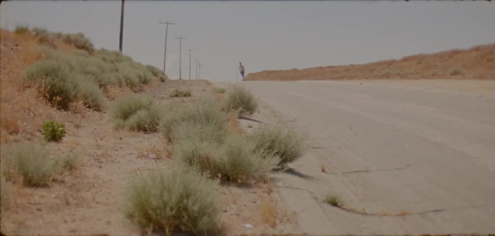Man skateboards along highway through arid scrub land