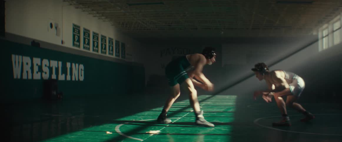 A pair of wrestlers wrestle in a dimly lit wrestling gym during the day