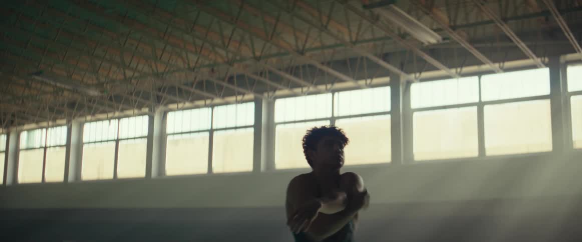 Young man standing in the middle of an empty gymnasium stretching his arms and shoulders