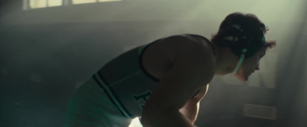 A pair of wrestlers compete in a dimly lit gym during the day
