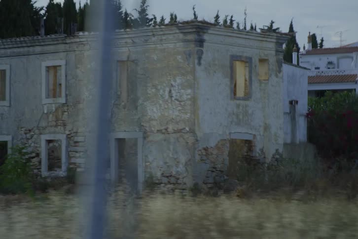 A shot of a decaying stone building on the edge of a forest as seen from a moving vehicle