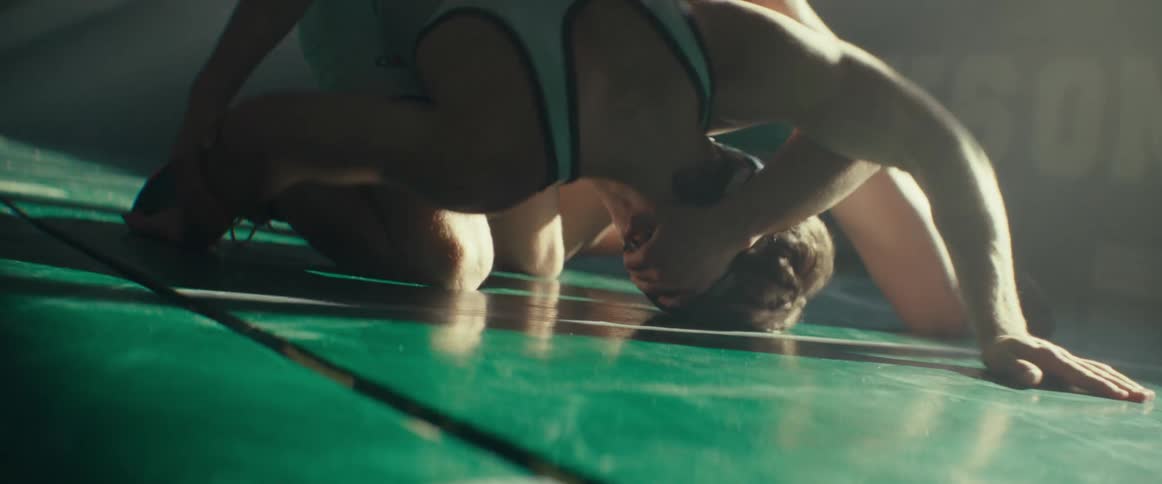 Two young men wearing wrestling clothes practicing wrestling in the middle of an empty gym during the day