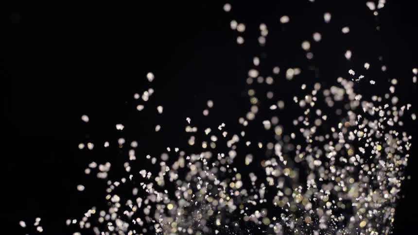 Pale particles fly through black glintingagainst the darkness